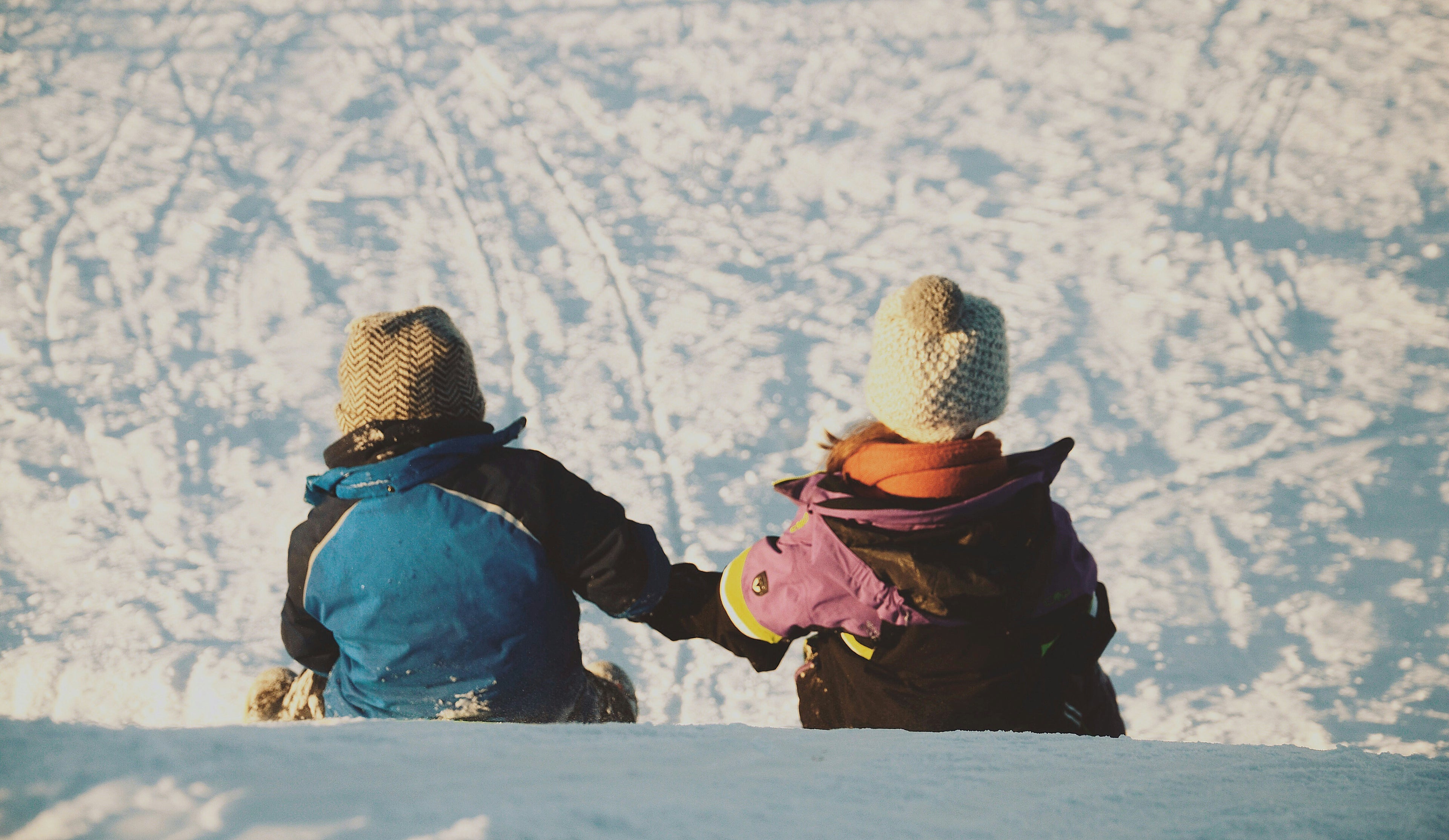 2 kids sliding down a snowy hill